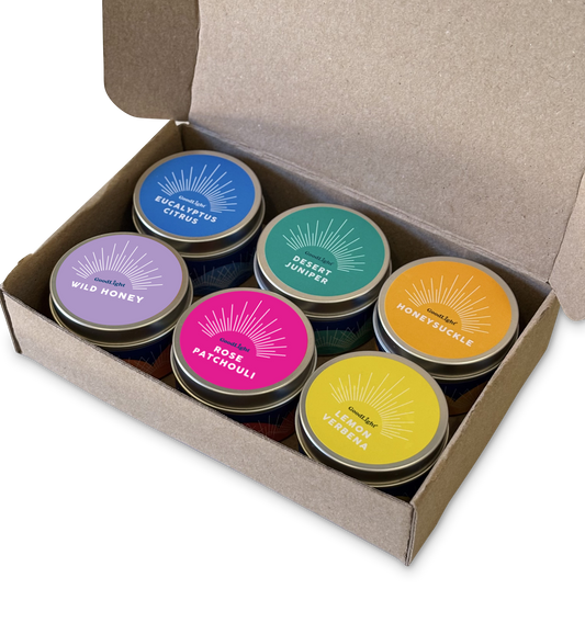 Set of colorful candle tins in a cardboard box on a white background.