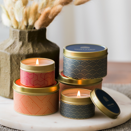 Stack of candles in decorative tins on a marble surface with a blurred background.