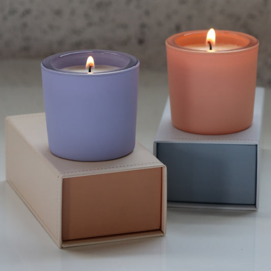 Two lit candles in colorful containers on geometric blocks with a neutral background