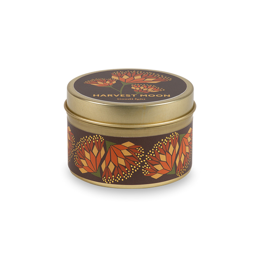 A round metal gold tin candle with a gold lid and base, featuring an autumnal label decorated with orange and pink flowers. The text on the lid reads "Harvest Moon" with GoodLight branding.
