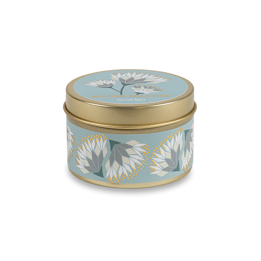 A round metal gold tin candle with a gold lid and base, featuring a light blue label decorated with cream and white flowers. The text on the lid reads "Winter Solstice" with GoodLight branding.