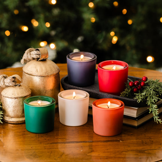 Colorful votive candles on a wooden surface with a blurred Christmas tree in the background.