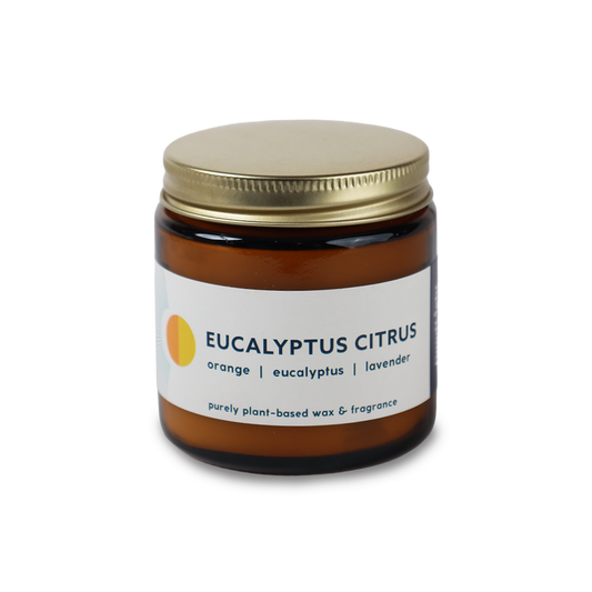 An amber glass jar candle with a gold metal lid and a white label reading 'EUCALYPTUS CITRUS' with orange and lavender scent notes, on a plain white background.