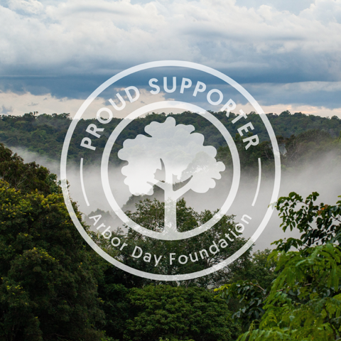A scenic landscape photo of a misty green forest under a cloudy sky, with a large white circular logo overlay reading, "Proud Supporter - Arbor Day Foundation" and a tree silhouette in the center.