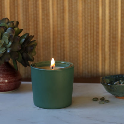 Green votive in front of a succulent and a bowl on a marble surface