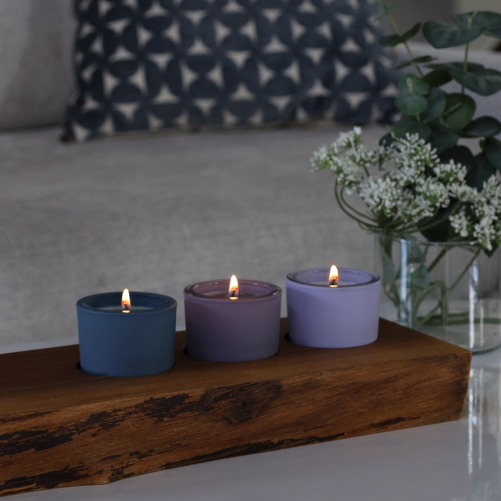 Three lit votive candles in blue and purple holders on a wooden surface with a blurred background