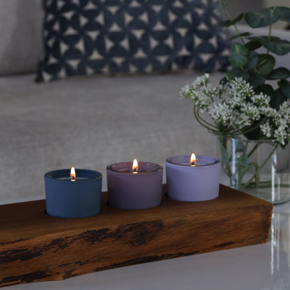 Three lit votive candles in blue and purple holders on a wooden surface with a blurred background
