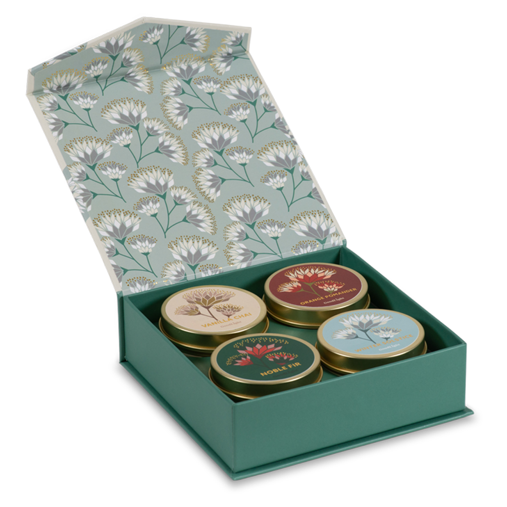 An open green gift box with a floral-patterned lid containing four small round tea tins. The tins have illustrated labels and are arranged in a clean studio shot on a white background.