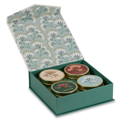 An open green gift box with a floral-patterned lid containing four small round tea tins. The tins have illustrated labels and are arranged in a clean studio shot on a white background.