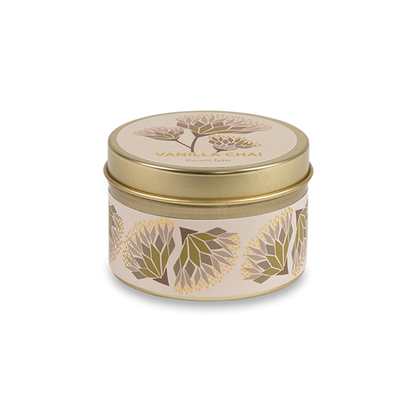 A round metal gold tin candle with a gold lid and base, featuring a cream label decorated with green, purple, and white flowers. The text on the lid reads "Vanilla Chai"  with GoodLight branding. 