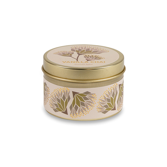 A round metal gold tin candle with a gold lid and base, featuring a cream label decorated with green, purple, and white flowers. The text on the lid reads "Vanilla Chai"  with GoodLight branding. 