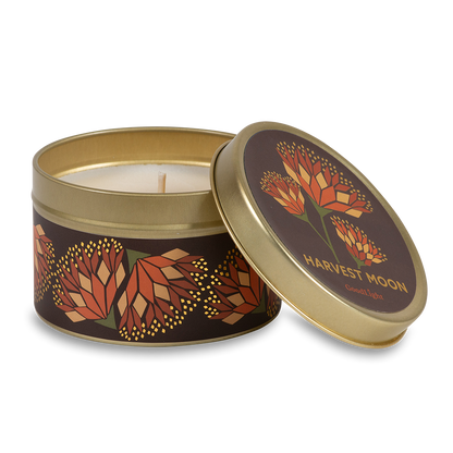 A round metal gold tin candle with a gold lid and base, featuring an autumnal label decorated with orange and pink flowers. The text on the lid reads "Harvest Moon"  with GoodLight branding. 