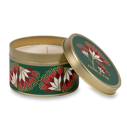 A round metal gold tin candle with a gold lid and base, featuring a green label decorated with red and pink flowers. The text on the lid reads "Noble Fir"  with GoodLight branding. 