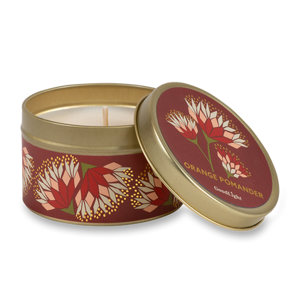 A round metal candle tin with the lid off, showing a white wax candle inside. The tin and lid feature a deep red background with an orange and cream floral pattern and gold lettering that reads "Orange Pomander" with GoodLight branding.