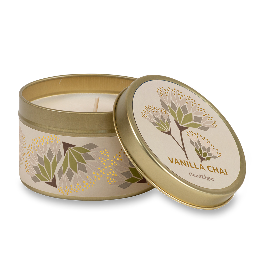 A round metal gold tin candle with a gold lid and base, featuring a cream label decorated with green, purple, and white flowers. The text on the lid reads "Vanilla Chai"  with GoodLight branding. 