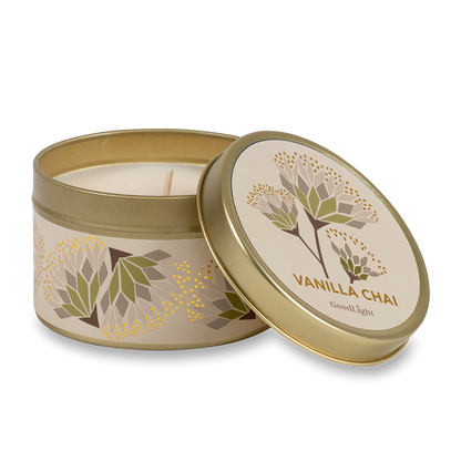A round metal gold tin candle with a gold lid and base, featuring a cream label decorated with green, purple, and white flowers. The text on the lid reads "Vanilla Chai"  with GoodLight branding. 