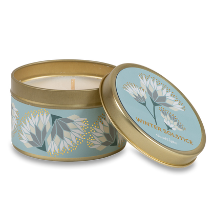 A round metal gold tin candle with a gold lid and base, featuring a light blue label decorated with cream and white flowers. The text on the lid reads "Winter Solstice"  with GoodLight branding. 