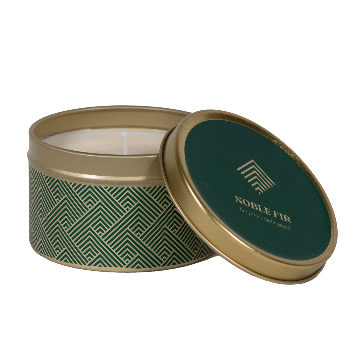 A round metal candle tin with its lid leaning against the base, showing a white candle inside. The tin has a dark green and gold geometric pattern on the body, and the lid features a dark green top with gold text reading "Noble Fire."