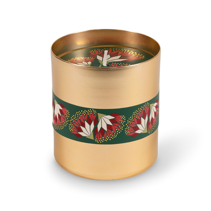 A cylindrical gold metal candle tin with a dark green band decorated with red and white floral motifs, shown on a clean white background.