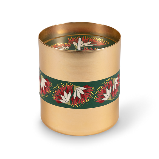 A cylindrical gold metal candle tin with a dark green band decorated with red and white floral motifs, shown on a clean white background.