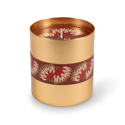 A cylindrical gold metal candle tin with a dark red band decorated with red and white floral motifs, shown on a clean white background.