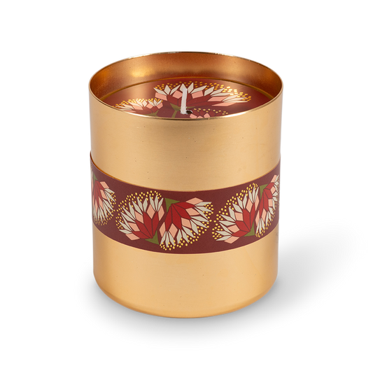 A cylindrical gold metal candle tin with a dark red band decorated with red and white floral motifs, shown on a clean white background.
