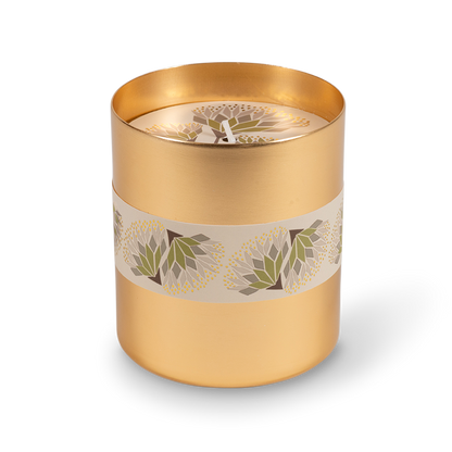 A cylindrical gold metal candle tin with a cream band decorated with green and white floral motifs, shown on a clean white background.