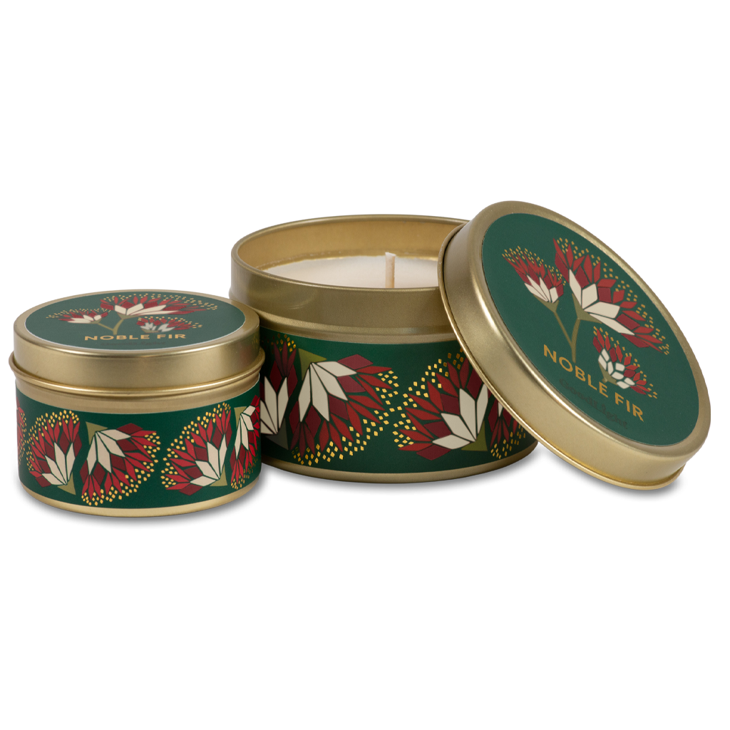 Two round metal tin candles with a festive green, red, and white leaf pattern and gold trim, shown on a clean white background. One tin is open, revealing the white wax inside, while the other one is closed.