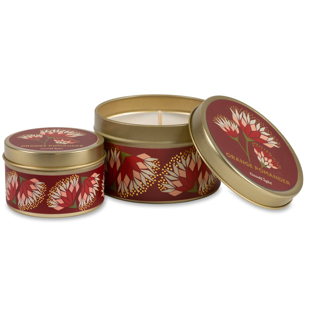 Two round metal candle tins with gold rims and a deep red label featuring orange and cream floral motifs. One tin is open, showing the white wax and wick, while the other is closed. 