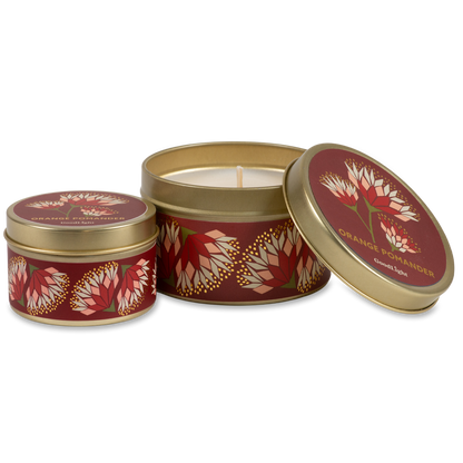 Two round metal candle tins with gold rims and a deep red label featuring orange and cream floral motifs. One tin is open, showing the white wax and wick, while the other is closed. 
