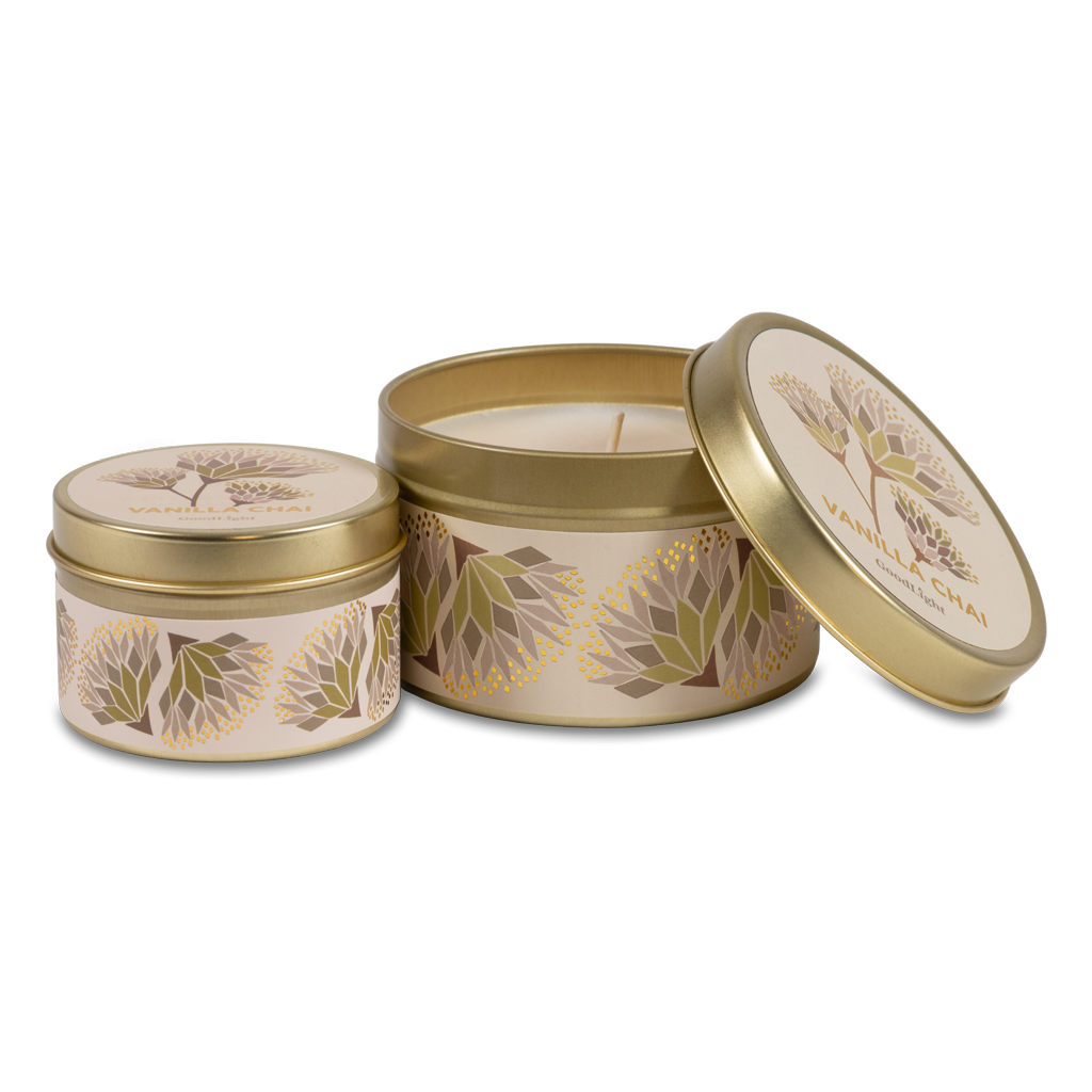 Two round metal candle tins with a gold finish and cream labels featuring botanical illustrations, set against a plain white background.