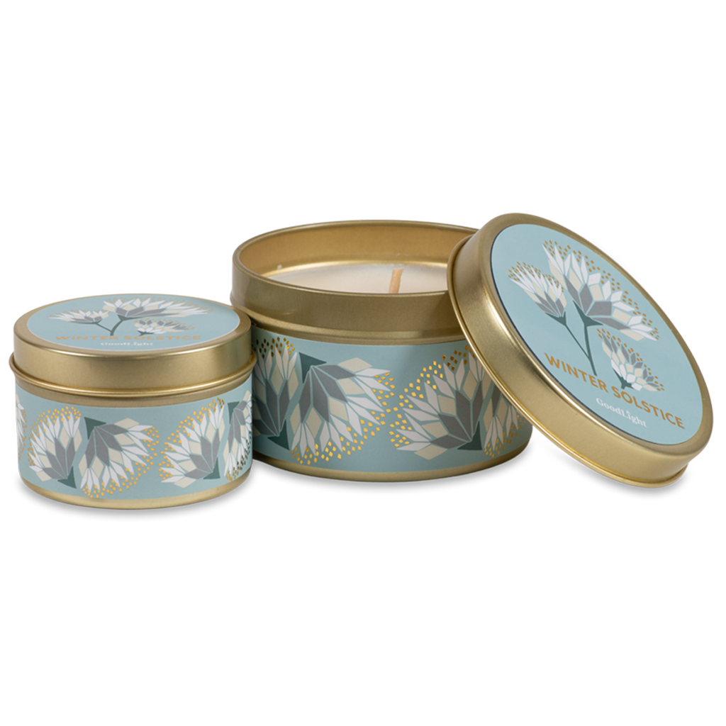 Two round metal candle tins with a light blue and white floral pattern and gold trim, shown on a clean white background. One tin is open, revealing a cream-colored wax candle inside, while the other is closed.