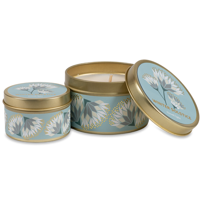 Two round metal candle tins with a light blue and white floral pattern and gold trim, shown on a clean white background. One tin is open, revealing a cream-colored wax candle inside, while the other is closed.