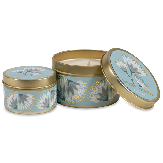 Two round metal candle tins with a light blue and white floral pattern and gold trim, shown on a clean white background. One tin is open, revealing a cream-colored wax candle inside, while the other is closed.